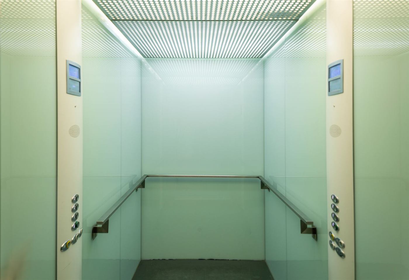 Intérieur d'une cabine d'ascenseur moderne aux parois claires et main courante en inox
