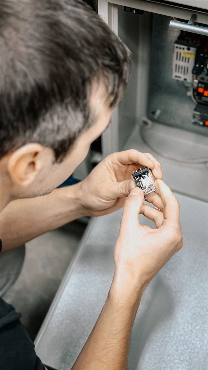 Technicien examinant une pièce électronique devant une armoire de commande
